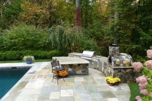 Earthscapes custom outdoor living service of a grill, barbeque pit, and outdoor kitchen with beautiful masonry work surrounding the pool area